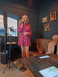 Jayne Darling performs her 1960s show wearing orange knee high boots and a purple and orange mini dress