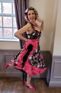 Jayne Darling is shown in a dancing pose with a black floral dress, pink shoes and a pink underskirt