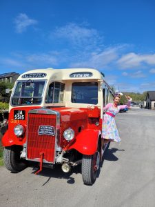 Jayne Darling is pictured in a floral dress leaning out the side of a vintage bus . It is sunny with blue skies