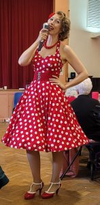 Jayne Darling in shown in a red and white polka dot Vivien of Holloway dress with red shoes - she is holding a vintage microphone