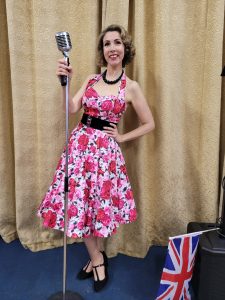 Jayne Darling is shown wearing a pink Vivien if Holloway dress with black belt, holding a vintage style microphone